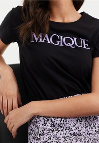 Černé bavlněné tričko s nápisem "MAGIQUE" v světle fialové barvě, spárované s purpurovou a černě tečkovanou sukní.