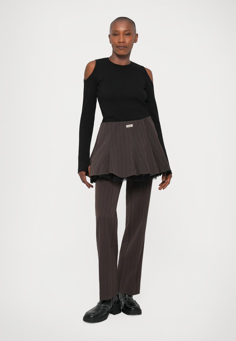 Zwart langslievend top met schouderuitsparingen, gecombineerd met een bruin gestreepte rok en bijpassende bruine broek. Zwarte schoenen maken de outfit compleet.