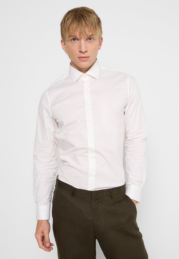 Witte longsleeve shirt met een klassieke kraag en knoopsluiting aan de voorkant, gecombineerd met donkergroene broeken met een effen textuur. Slank ontwerp.
