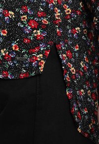 Svart blommig blus med röda, blå och gula blommor, med ett prickigt mönster; inkluderar en sidoflagg och en liten metallskylt.