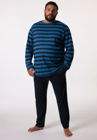 Camisa de rayas azul de manga larga con rayas negras y escote redondo, combinada con pantalones oscuros; tela suave, corte relajado y sin patrones visibles.