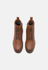 Bottines en cuir marron avec un laçage à l'avant, une fermeture éclair sur le côté et des détails texturés sur le dessus. Finition lisse et design à bout rond.