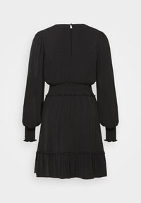 Robe noire à manches longues avec taille smockée, ourlet et poignets à volants, et une petite ouverture boutonnée au niveau de l'encolure arrière, vue de dos.