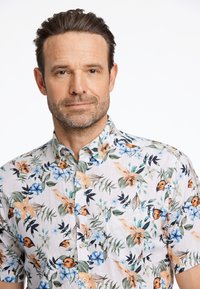 Camicia a maniche corte con sfondo bianco e motivi florali e fogliari multicolori. Include un colletto a bottoni e una tasca sul petto.