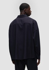Granatowa koszula overshirt w paski o luźnym kroju, z kołnierzykiem w kształcie punktu, długimi rękawami i mankietami zapinanymi na guziki, uszyta z gładkiego materiału.
