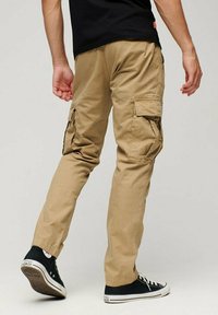 Pantaloni cargo khaki con più tasche laterali, design a gamba dritta, materiale cotone e texture liscia, indossati con sneakers nere.