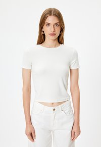 Hvid t-shirt med korte ærmer, rund hals, tætsiddende design og glat tekstur, bæres med matchende hvide højtaljede jeans.