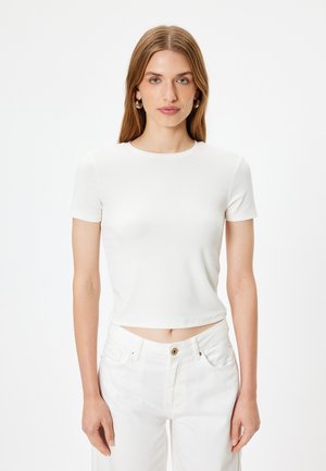 Hvid t-shirt med korte ærmer, rund hals, tætsiddende design og glat tekstur, bæres med matchende hvide højtaljede jeans.