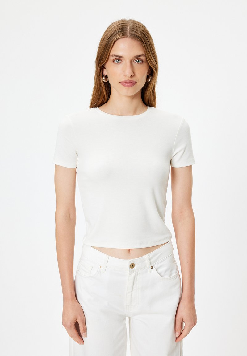 Hvid t-shirt med korte ærmer, rund hals, tætsiddende design og glat tekstur, bæres med matchende hvide højtaljede jeans.