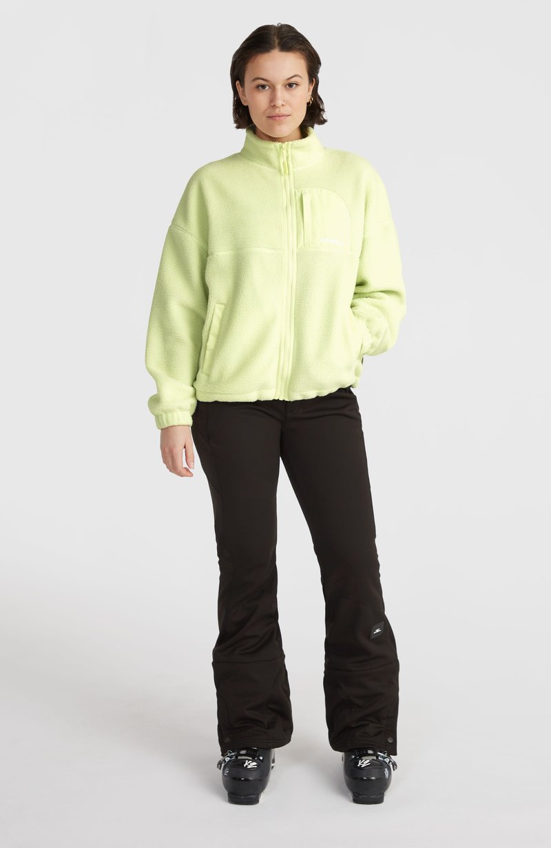 Hellgrüne Fleecejacke mit Reißverschluss, hohem Kragen und Fronttasche. Kombiniert mit schwarzen Skihosen und Stiefeln, was einen winterlichen Look kreiert.