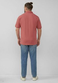 Kurzärmliges, korallenfarbenes Poloshirt mit Kragen, kombiniert mit hellblauen Jeans und weißen Sneakers. Lässige Passform; keine sichtbaren Muster.