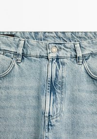 Ljusblå denimjeans med en urblekt textur, ett knappstängning och vanliga fickor. Har sömnadsdetaljer och en avslappnad passform.