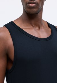 Μαύρο αμάνικο μπλουζάκι από λείο βαμβακερό ύφασμα, με στρογγυλή λαιμόκοψη και καθαρά ρα�μμένα τελειώματα, σε αθλητική γραμμή.