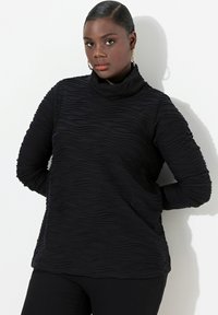 Schwarzes Langarmoberteil mit einem strukturierten, wellenförmigen Muster. Verfügt über einen Stehkragen und schmal geschnittene Ärmel. Hergestellt aus einem weichen, dehnbaren Material.