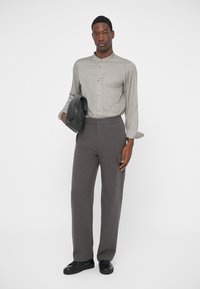 Grå mønstrete langermet skjorte, løstsittende grå bukser med sidelomme, og svart skinn clutch. Svarte sko fullfører antrekket.