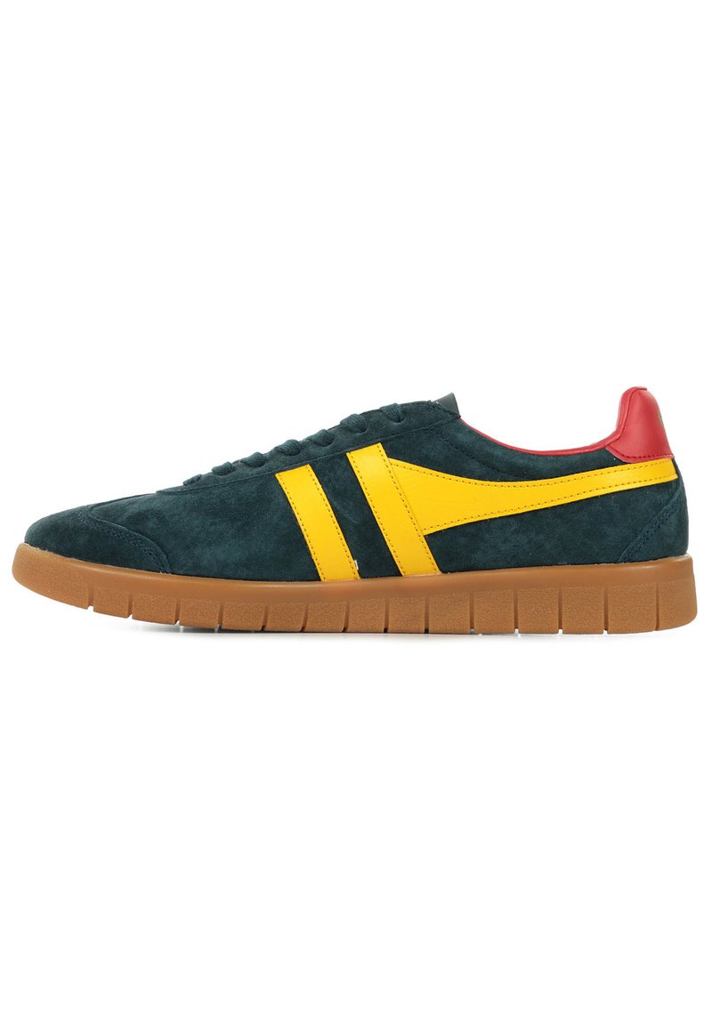Zapatillas de ante con un cuerpo verde oscuro, rayas laterales amarillas, una capucha del talón roja y una suela de goma marrón texturizada con ranuras horizontales.