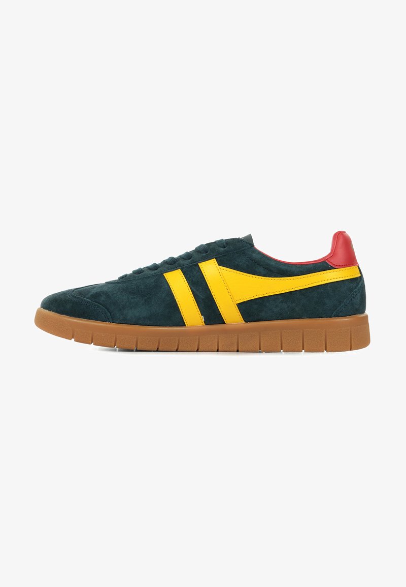 Zapatillas de ante con un cuerpo verde oscuro, rayas laterales amarillas, una capucha del talón roja y una suela de goma marrón texturizada con ranuras horizontales.