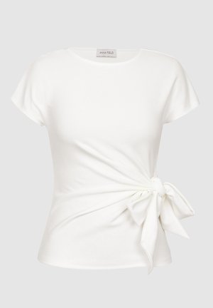 Vit kortärmad topp med rundhalsringning och detalj med sidoknyte. Tillverkad av mjukt tyg, med en figurnära passform.