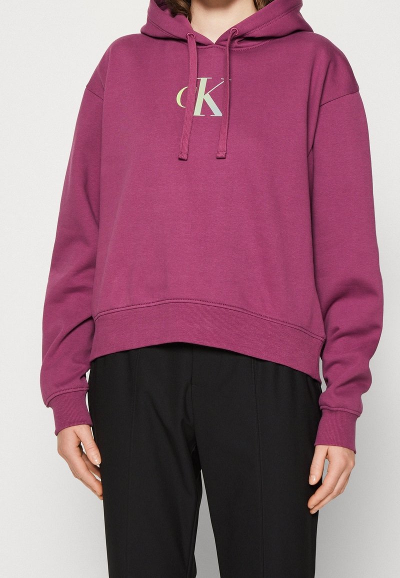 Fuchsia hooded sweatshirt with a cropped design, featuring a front logo in light colors and adjustable drawstrings at the neckline.