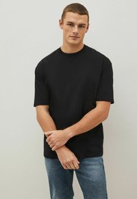 T-shirt nera a maniche corte in una vestibilità rilassata, realizzata in cotone. Presenta un colletto a girocollo e una texture liscia. Abbinata a jeans in denim di un blu chiaro.