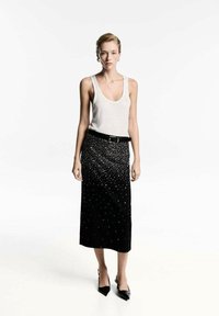 Fustă neagră ajustată, cu un model strălucitor, până la genunchi, asociată cu un top alb fără mâneci. Modelul poartă pantofi cu vârf ascuțit negri.