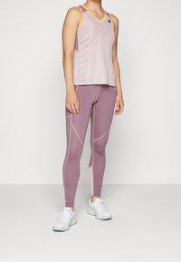 Top leggero senza maniche di un rosa pallido con pannelli in rete, abbinato a leggings lavanda a vita alta con cuciture a contrasto. Sneakers bianche.