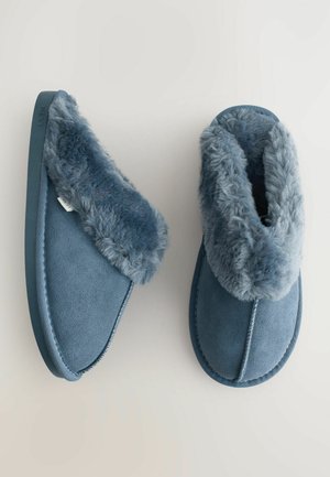 Sinised seemisnahast sussid võltskarvase mansetiga, ümarate vormidega ja tekstureeritud pinnaga. Omavad kontrastset õmblust ning painduvat kummist talda.