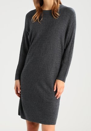 Robe gris foncé en maille avec texture côtelée, encolure ronde et manches longues légèrement amples. Dotée d'une fente latérale pour faciliter les mouvements.