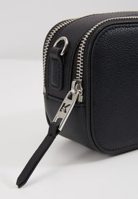 Borsa in pelle nera con texture, dotata di zip argentata, con un'etichetta brandizzata e una forma rettangolare compatta.
