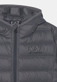 Szara kurtka puffa z kapturem, pikowany design, zamek błyskawiczny i czarne logo EA7 z przodu. Wykonana z błyszczącego, gładkiego materiału.