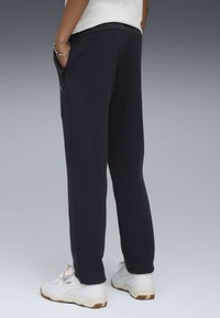 Marineblauwe joggingbroek van zacht materiaal, met zijzakken. Gekocht met witte sneakers. Zichtbaar logo-accent aan de linkerkant.