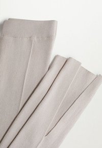 Žebrované světle béžové legíny s hladkým povrchem, opatřené širokým pasem a jemnými detaily švů. Prezentace na rovině.