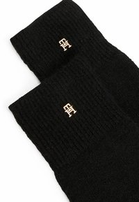Black knitted socks feature a ribbed texture and a small gold logo accent. The cuffs are thick and can be rolled down.
