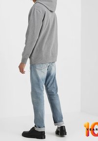 Šedá mikina s kapucí a přední kapsou, spárovaná se světle modrými tapered džíny a černými šněrovacími botami. Jednoduchý design a volný střih.