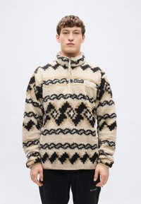 Πουλόβερ με γιακά σε μπεζ φλις με μαύρα και καφέ γεωμετρικά σχέδια. Διαθέτει φερμουάρ, τσέπη στο στήθος και ελαστικές μανσέτες.