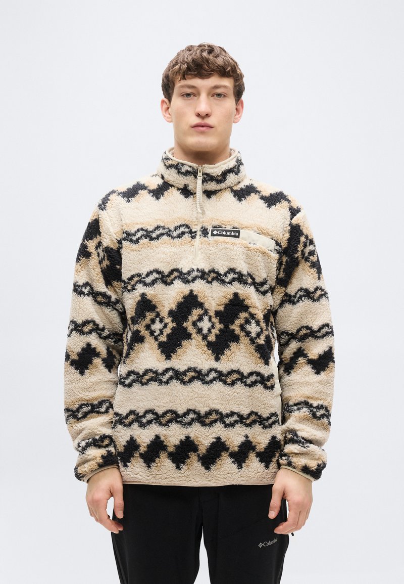 Πουλόβερ με γιακά σε μπεζ φλις με μαύρα και καφέ γεωμετρικά σχέδια. Διαθέτει φερμουάρ, τσέπη στο στήθος και ελαστικές μανσέτες.