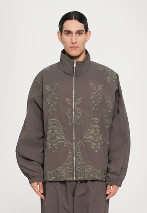 Gray jacket with high collar and zip closure. Features intricate green embroidery and oversized sleeves, made from smooth fabric.