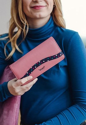 Pink leather wallet with a wavy black accent featuring colorful polka dots. Compact design held by a hand, set against a blue top.