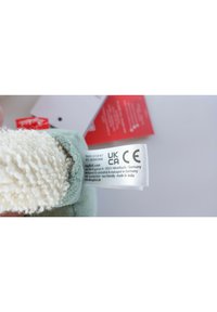 Weiches grünes Gewebe mit einer weißen, flauschigen Textur. Enthält ein Pflegeetikett mit UKCA- und CE-Kennzeichnungen. Rote und weiße Etiketten sind sichtbar.