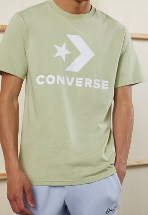 Jasnozielona bawełniana koszulka z krótkim rękawem, z dużym białym logo "Converse", gwiazdą i wzorem strzały z przodu. Okrągły dekolt.
