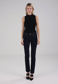 Svart ermeløs topp kombinert med mørkeblå skinny jeans. Jeansene har en rød knapp og subtil søm. Svart høye hæler fullfører looken.