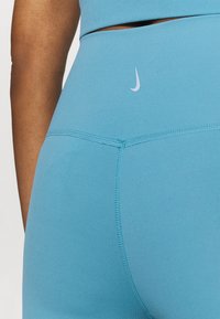 Hellblaue Sportleggings aus dehnbarem Stoff, mit einem kleinen weißen Logo am Bund und sichtbaren Nähdetails.