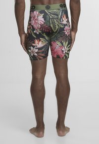 Męskie bokserki w kwiatowy wzór, z czarnym tłem oraz kolorowymi hibiskusami i liśćmi, elastyczny zielony pas w talii oraz dopasowany krój.