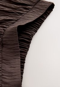 Gros plan d'un tissu marron foncé avec une texture froncée et un bord lisse et plié sur un fond clair.