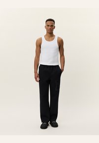 Hvid bomulds tanktop, sorte afslappede sweatpants med sidelomme-detalje og sorte slip-on sko. Enkelt baggrund.