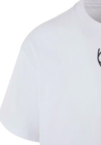 T-shirt blanc à manches courtes avec col rond présentant un texte partiel noir ou un motif près de la partie supérieure de la poitrine.