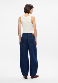 Φαρδιά τζιν παντελόνια σε σκούρο μπλε με ψηλή μέση, διαθέτοντας δύο πίσω τσέπες και μια καφέ δερμάτινη ετικέτα στη μέση.