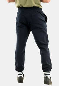 Pantalones de chándal azul marino con cinturilla elástica, bolsillos laterales y puños acanalados en los tobillos. Llevados con zapatos negros y calcetines a rayas blancas.