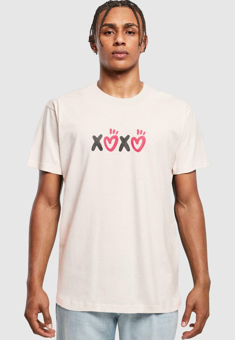 Lyserød bomulds t-shirt med et centralt grafisk motiv med "XOXO" tekst i sort og lyserød, samt håndtegnede detaljer i rød. Korte ærmer.