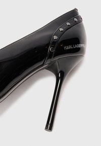 Pantofi cu toc stilletto din piele lacuită neagră, cu cuie argintii de-a lungul marginii și cu branding "KARL LAGERFELD" pe lateral.